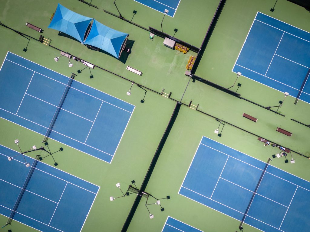 Aerial view of blue tennis courts with green surrounds
