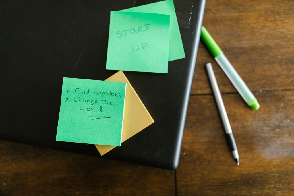 Green sticky notes with startup goals on a wooden desk with pens