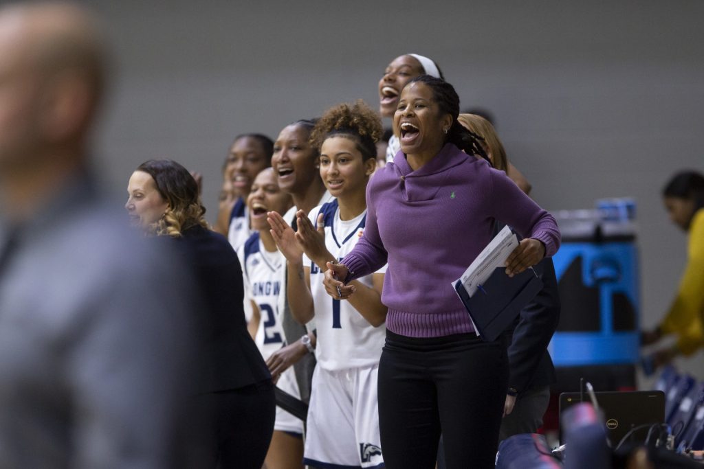 Coach in a purple top speaking with women basketball players on court